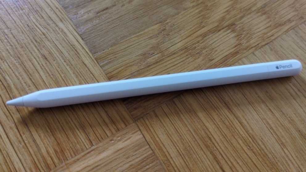 Digitaler Eingabestift in Weiß auf gemustertem Holzboden, seitliche Perspektive.